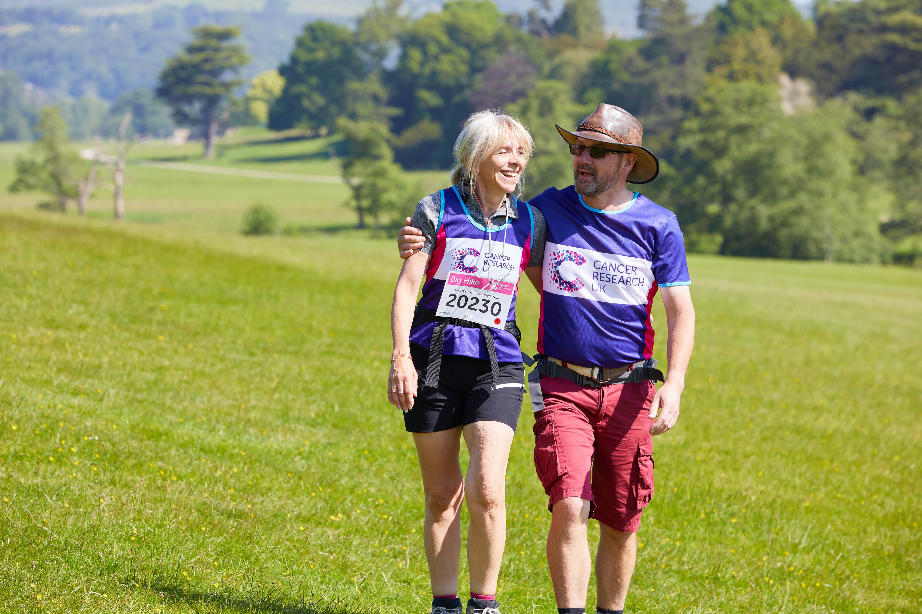 man and a woman with their arms around each other walking in the countryside.