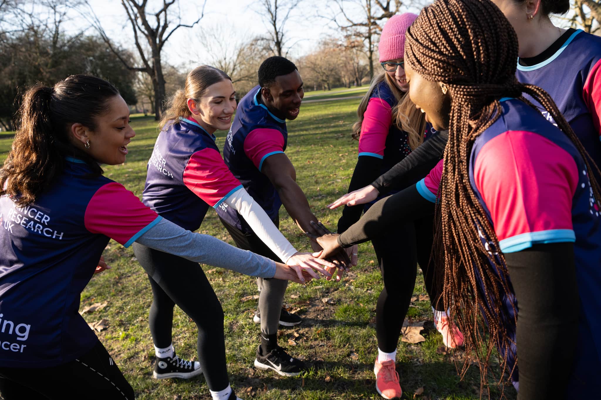 A photo of a group of people wearing Cancer Research UK t-shirts putting their hands together in a team huddle.