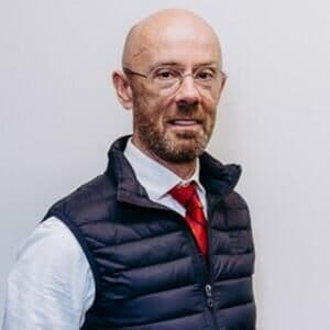 A smartly dressed man with glasses and a beard smiling.