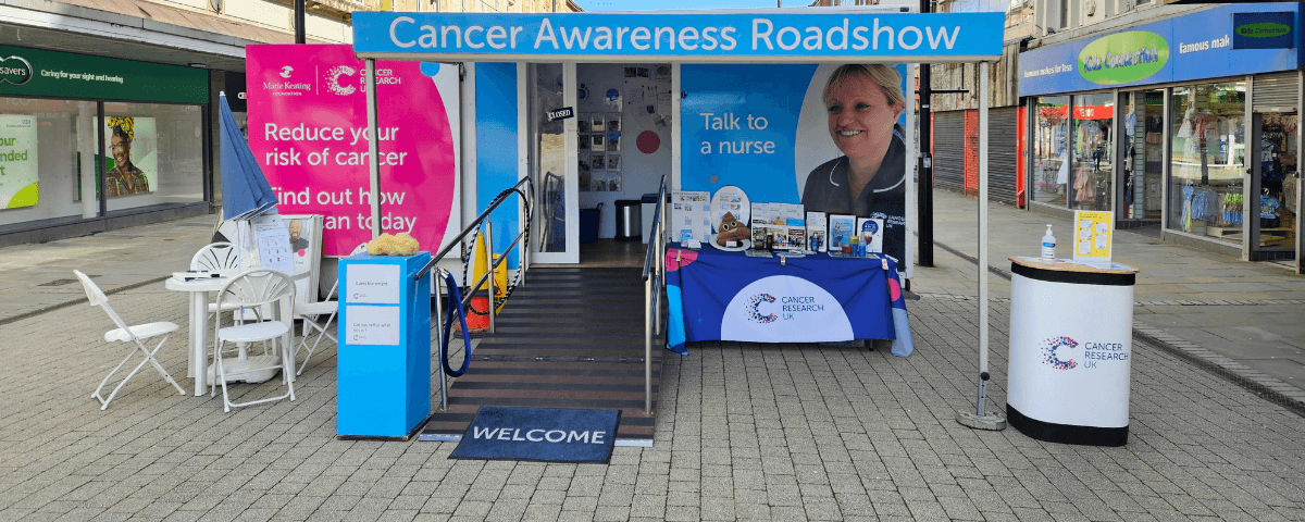 A photo of the Cancer Awareness Roadshow stand surrounded by shops.