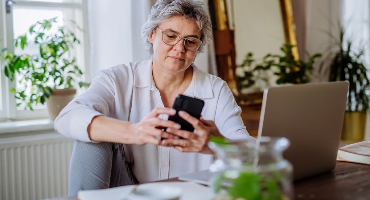 Image shows volunteer sat at a table using mobile phone and laptop.