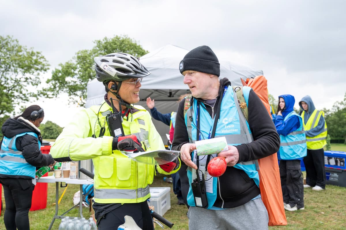 Two volunteers talking to each other at a sports event, looking at a map.