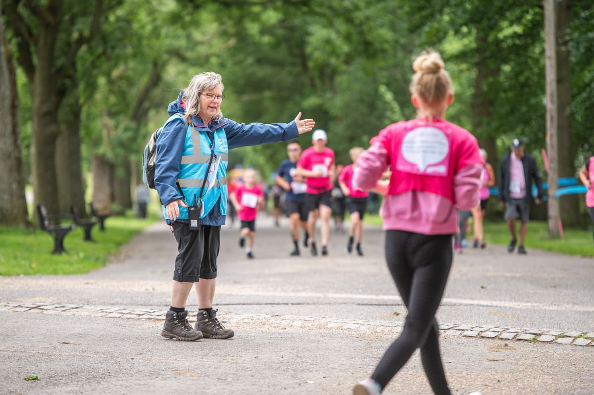 A female volunteer at a Race for Life event showing a runner the direction.