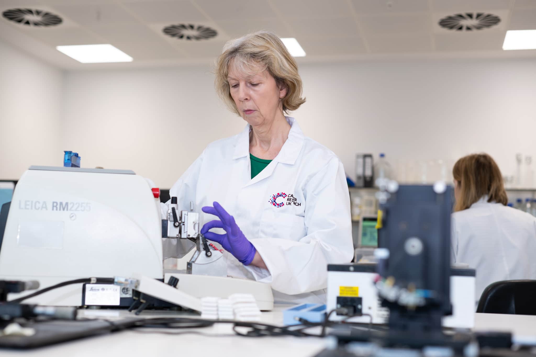 A researcher working in the lab with a white lab coat with the Cancer Research UK logo.