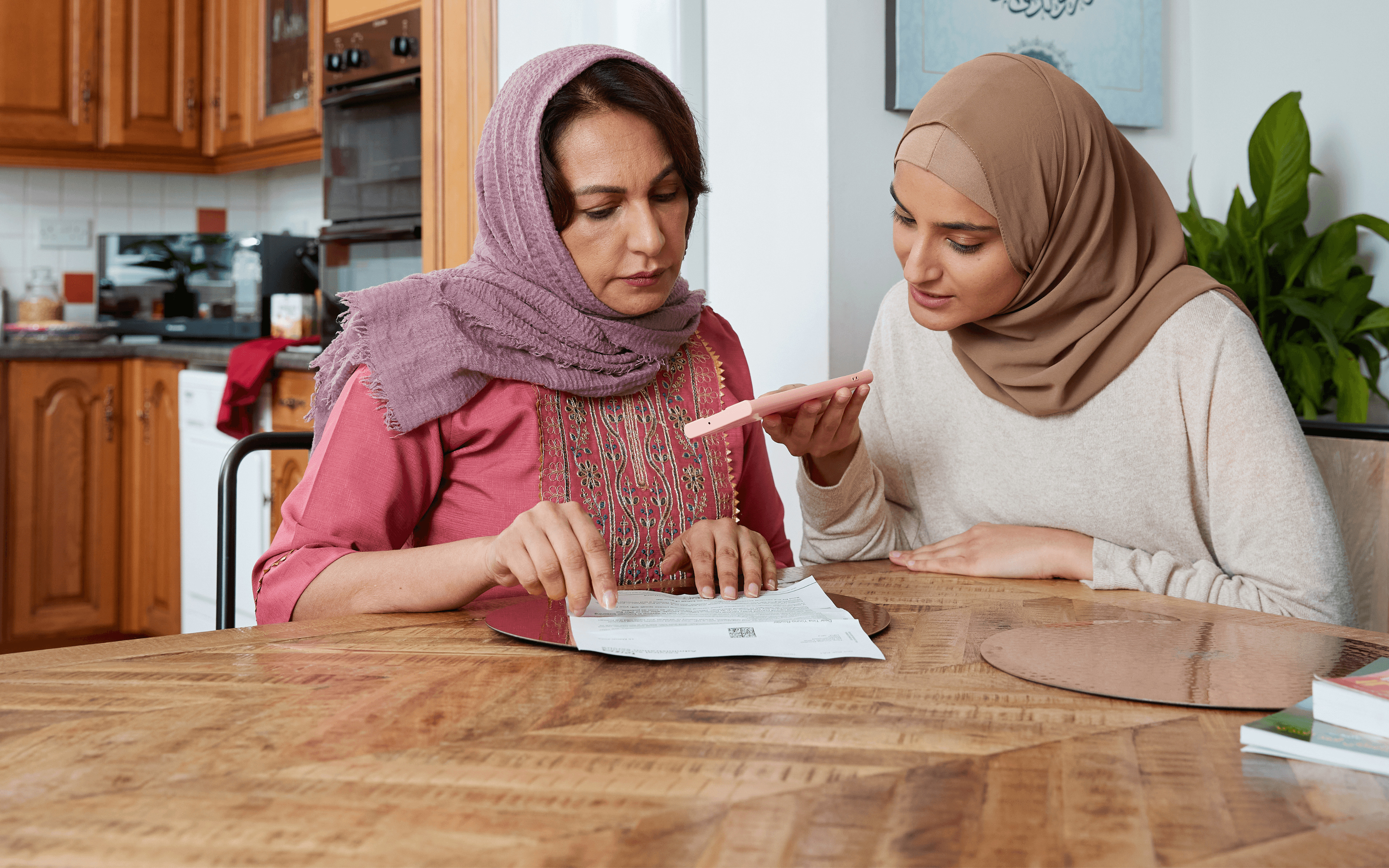 A daughter helping her mother to book a routine cervical or breast screening appointment on the phone in the kitchen.