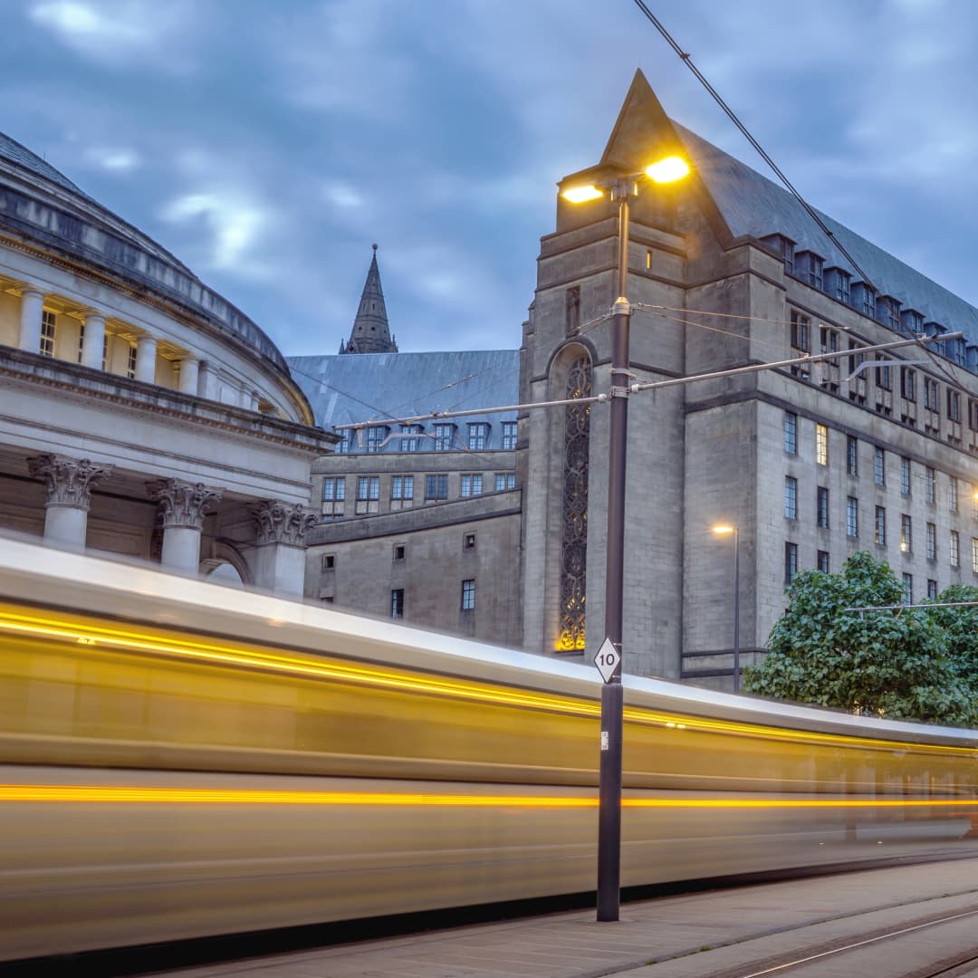 Photograph of a train passing by historic buildings in Manchester at sunset.