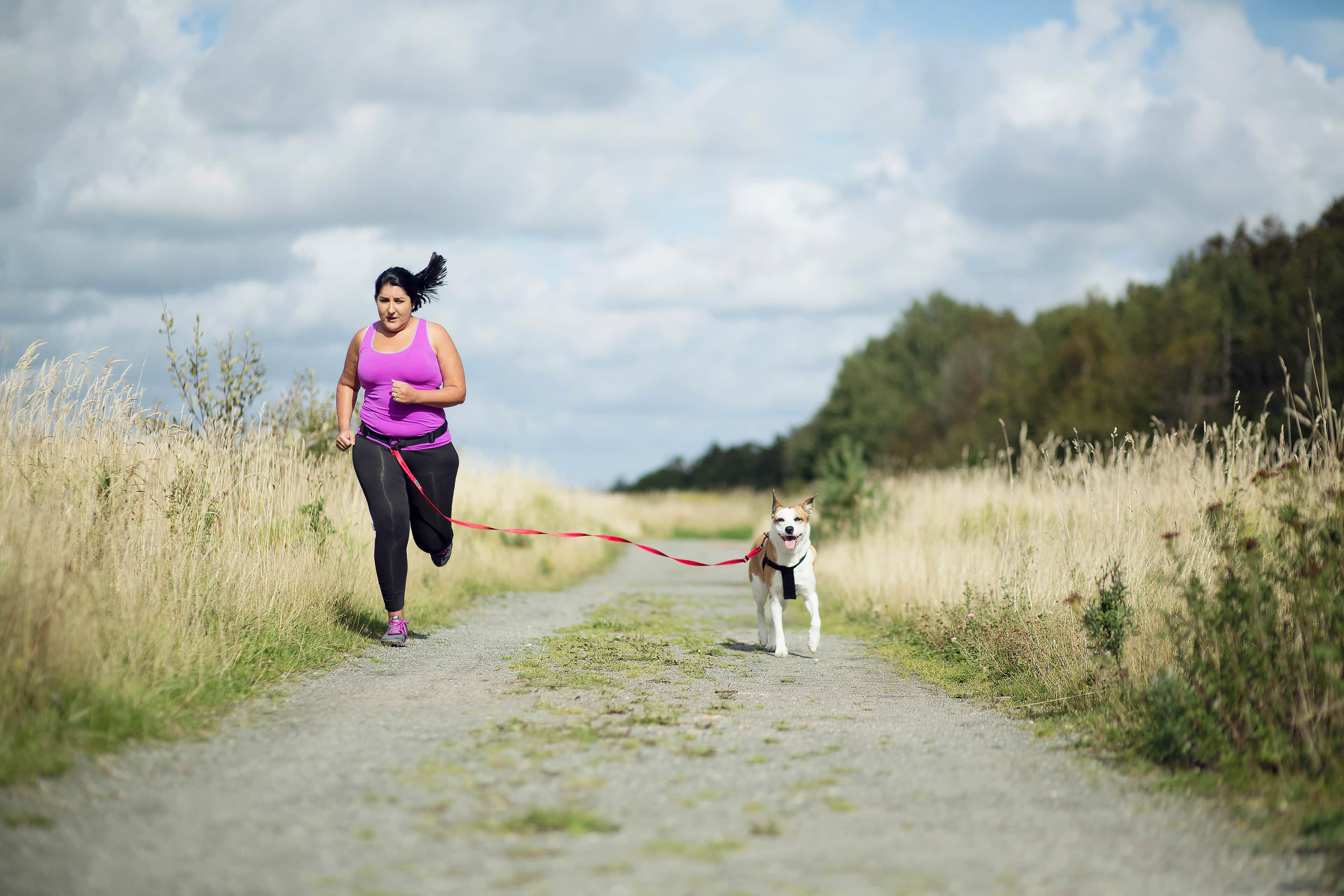 A woman jogging with her dog along a grassy countryside.