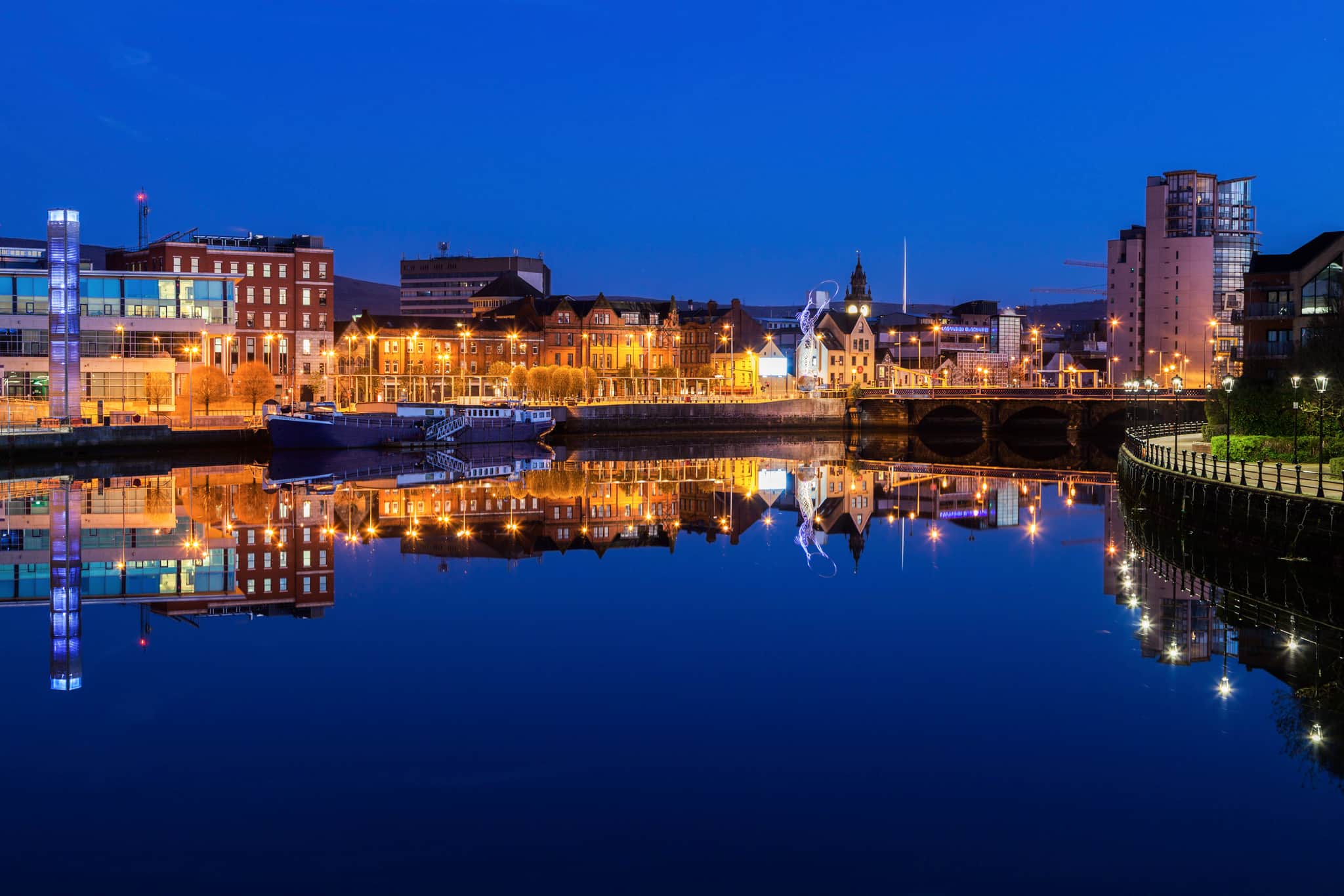 Belfast at night with lights from the buildings reflected in the River Lagan.