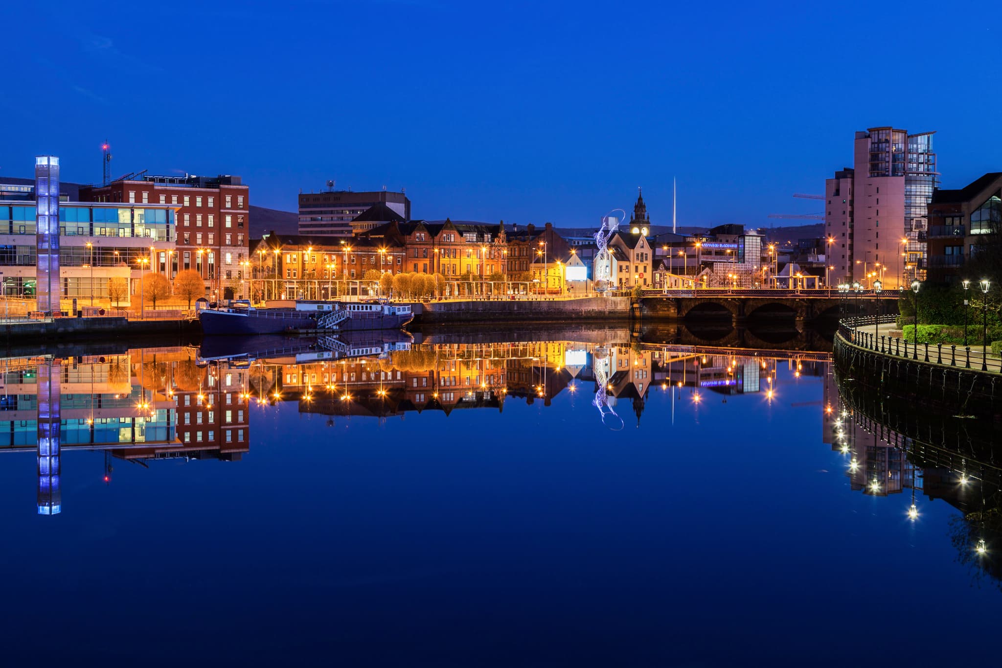 Belfast at night with lights from the buildings reflected in the River Lagan.