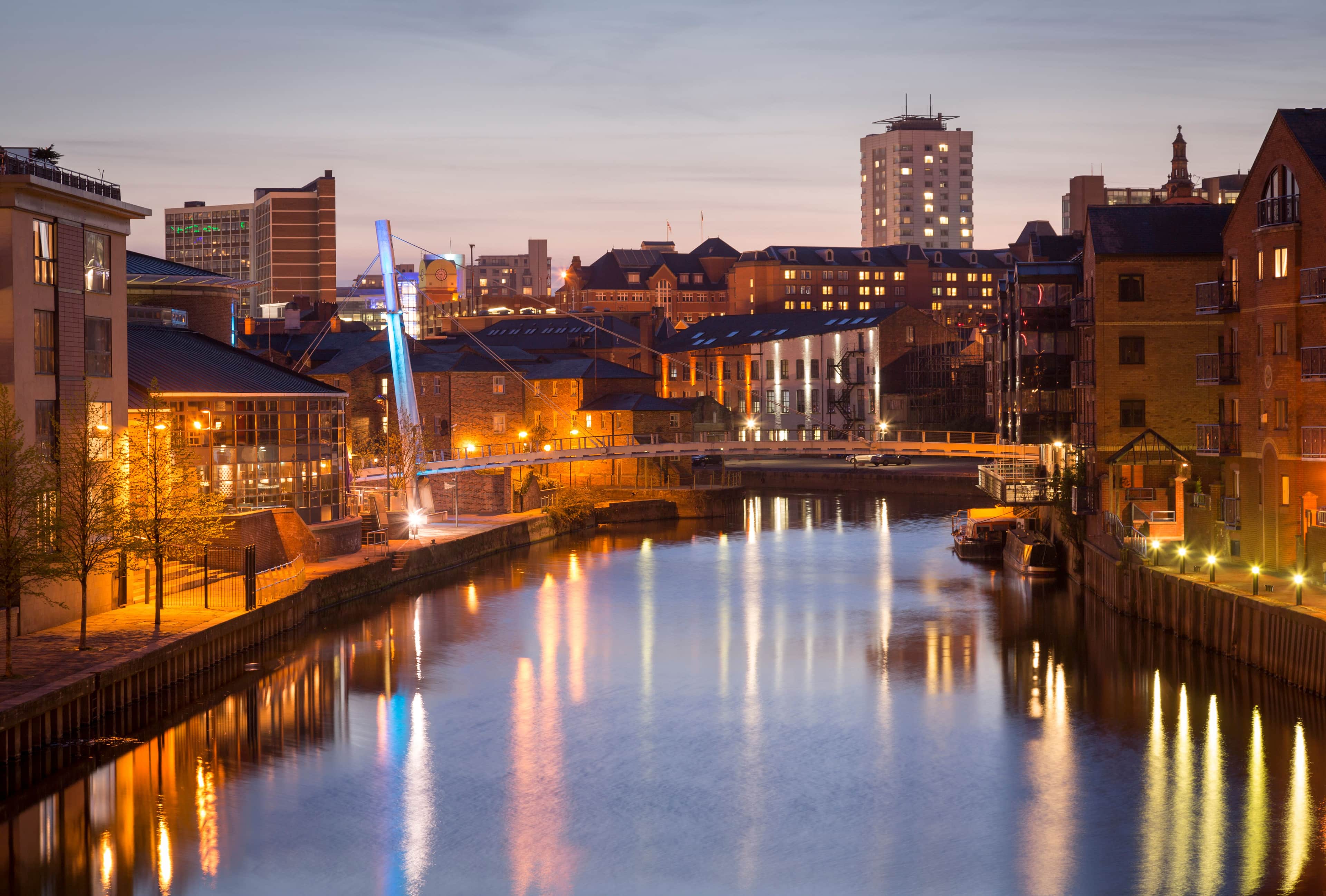 The image depicts a nighttime view of Leeds city centre waterfront in England.