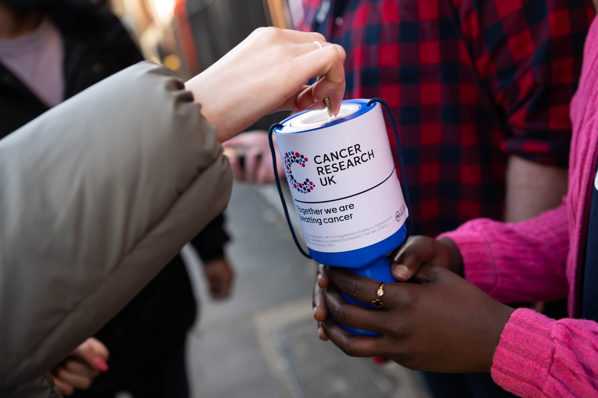 A person holding out a Cancer Research UK donation goblet and someone putting a donation in it.