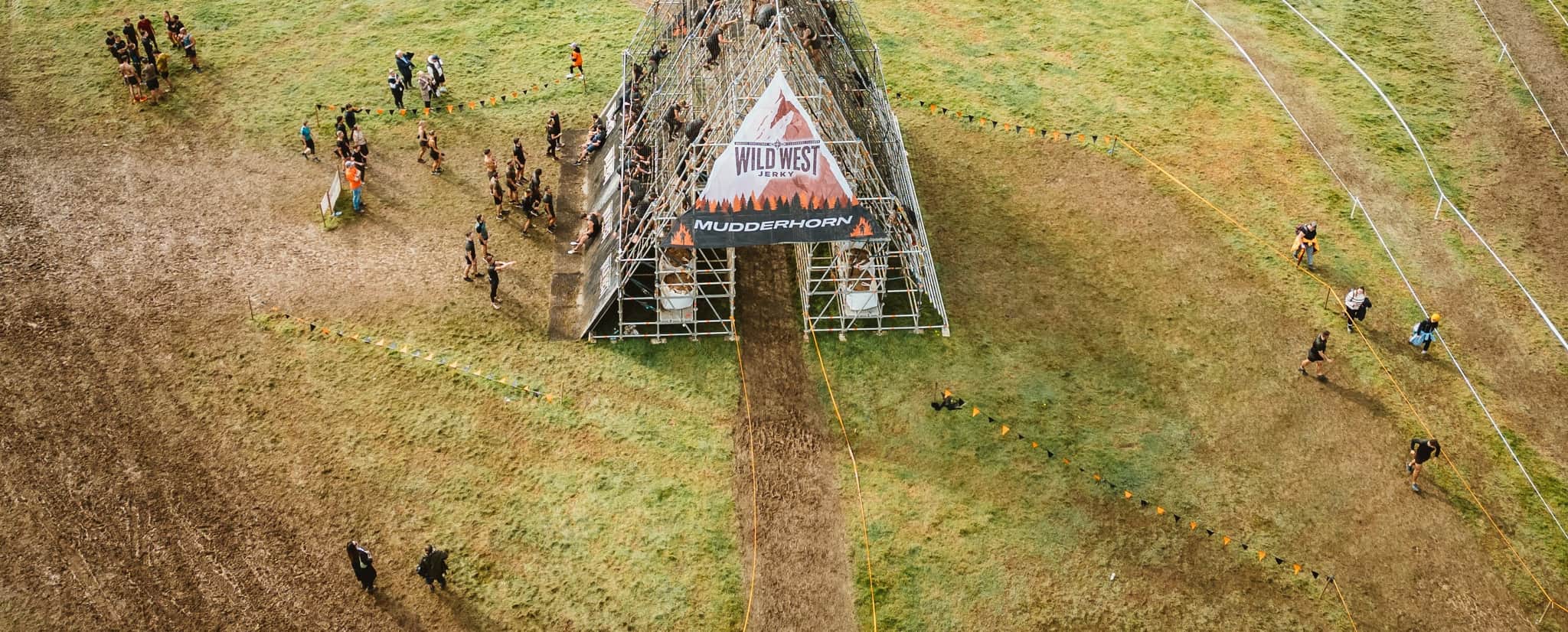people in the middle of a green field climbing up and going down a metal house shaped structure.