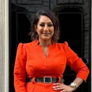 A smiling, smartly dressed woman stands in front of a door.