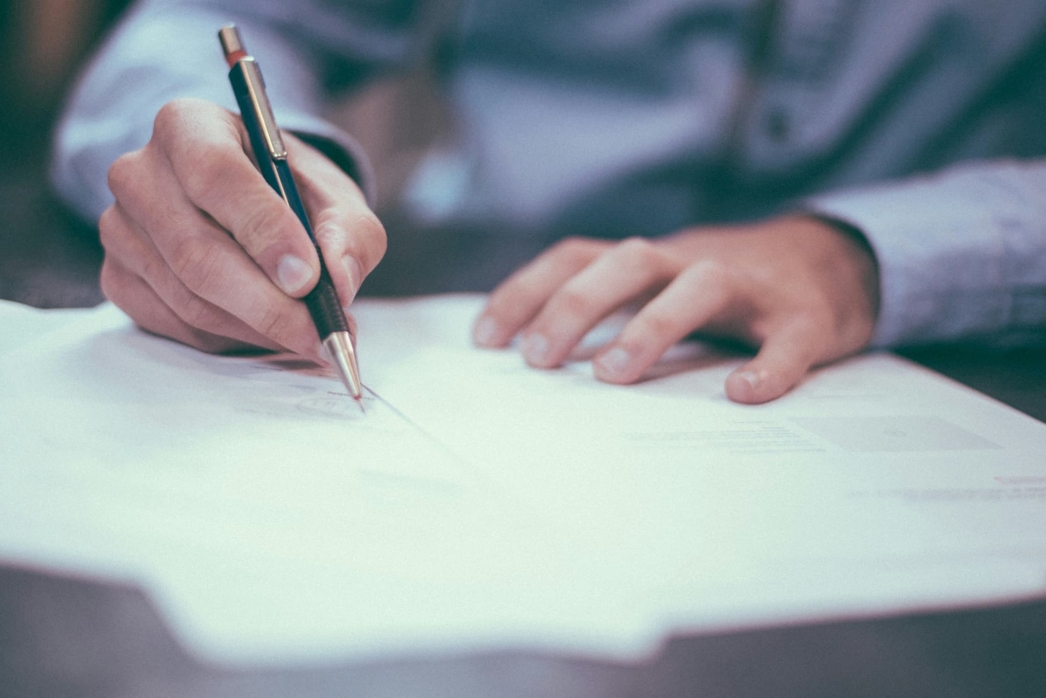 A man's hands are seen writing on a document with a roller ball pen.