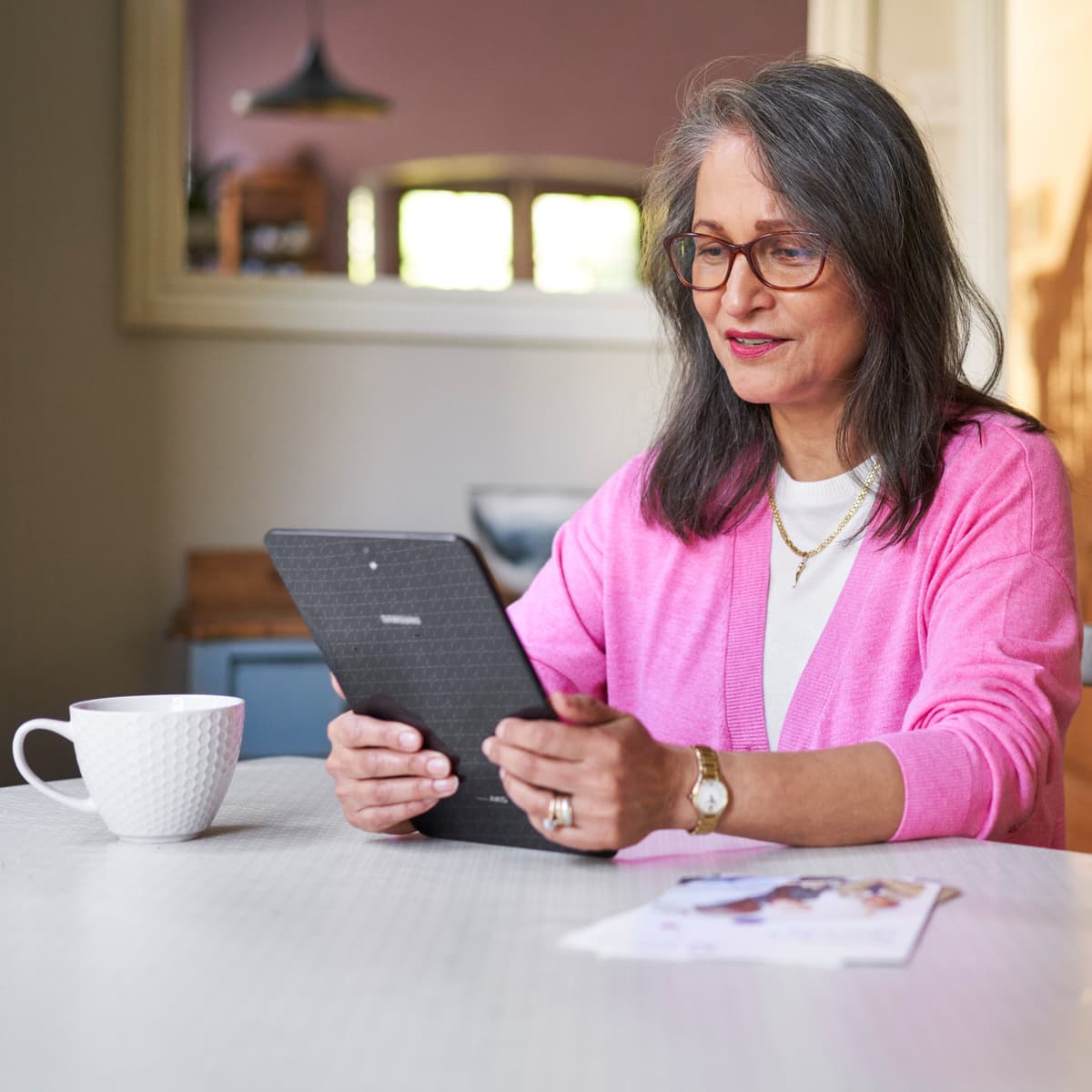 Image of a woman sat at her dining room table looking at her computer tablet.
