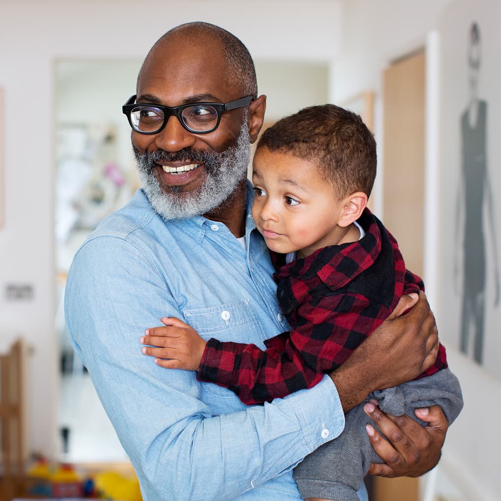 Man smiling holding young grandson.